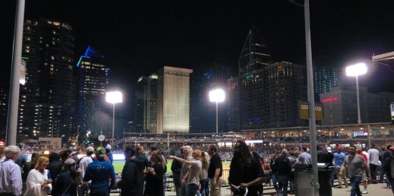 Crowd at a floodlit ballpark in Charlotte at night with the lit Uptown skyline rising behind