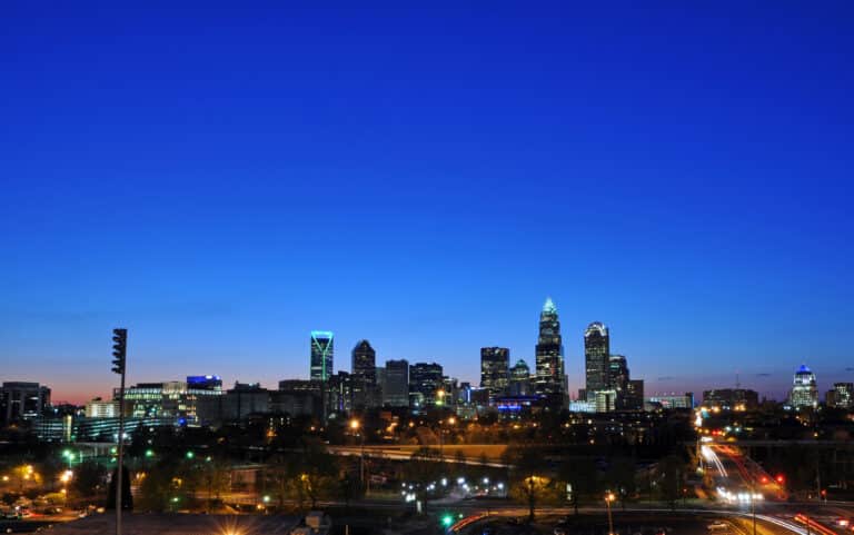The Uptown Charlotte skyline lit up at blue hour beneath a deep blue evening sky