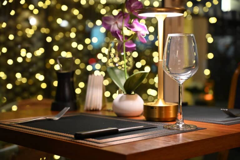 Candlelit restaurant table set for dinner with a wine glass and orchid against warm bokeh lights