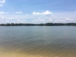 Summer view across Lake Norman from the shallow sandy shoreline at Ramsey Creek Park, with wooded far bank and blue sky